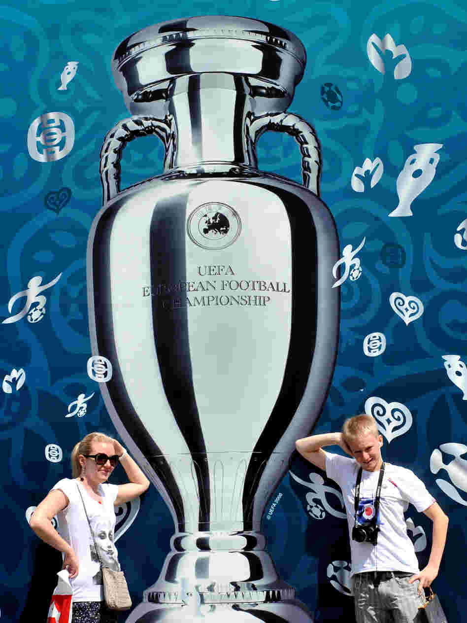 Larger Than Life: Tourists pose in front of a UEFA Euro 2012 Cup placard on Kiev's Independence Square in Ukraine. Europe is entering a packed sports schedule — but soccer still reigns supreme, says Frank Deford.