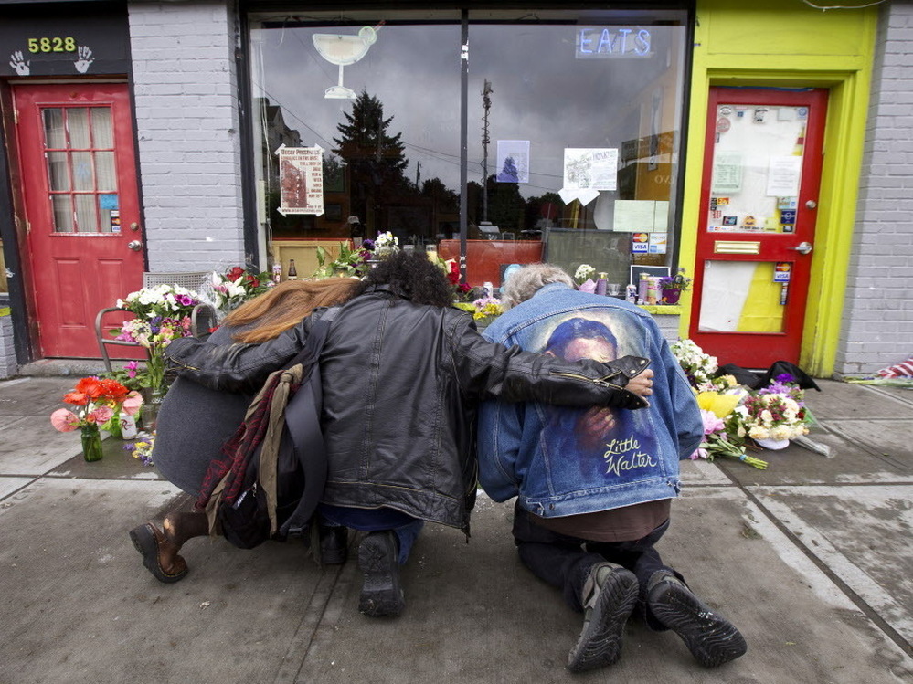 Left to right: Karen Eides, Tim Torres and David Gordon embrace as they kneel in front of a makeshift memorial outside the cafe in Seattle where a gunman killed four people.