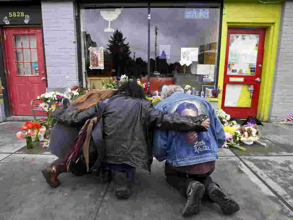 Left to right: Karen Eides, Tim Torres and David Gordon embrace as they kneel in front of a makeshift memorial outside the cafe in Seattle where a gunman killed four people.