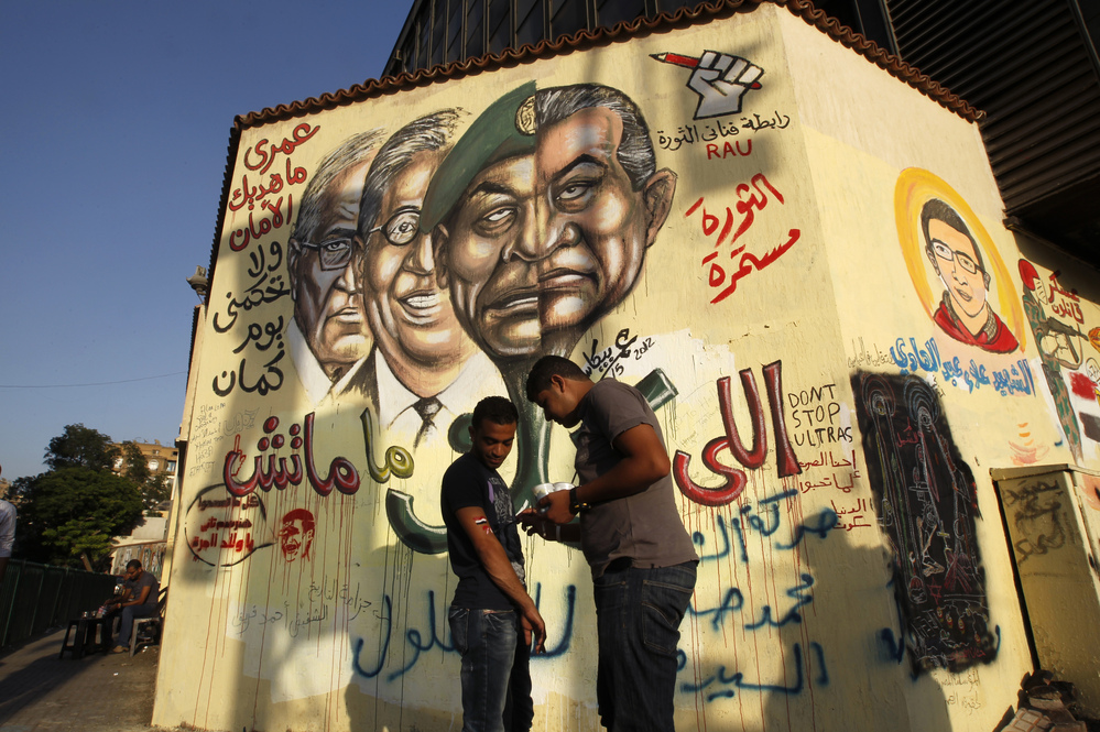 An Egyptian man paints the national flag on the arm of a friend as they stand in front of graffiti showing the morphed faces of ousted Egyptian President Hosni Mubarak (right) and military ruler Hussein Tantawi, defeated presidential candidate Amr Moussa (second from left), and current candidate Ahmed Shafiq (left) near Cairo's central Tahrir Square last month.