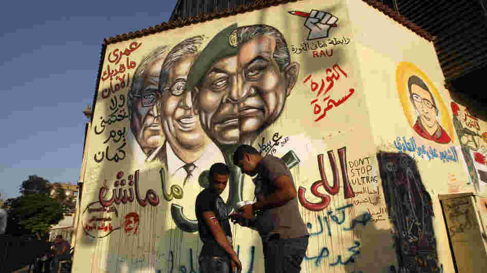An Egyptian man paints the national flag on the arm of a friend as they stand in front of graffiti showing the morphed faces of ousted Egyptian President Hosni Mubarak (right) and military ruler Hussein Tantawi, defeated presidential candidate Amr Moussa (second from left), and current candidate Ahmed Shafiq (left) near Cairo's central Tahrir Square last month.
