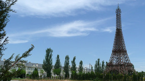 A rusting model of the Eiffel Tower stands at one end of the theme park, surrounded by construction debris and empty housing outside the park.