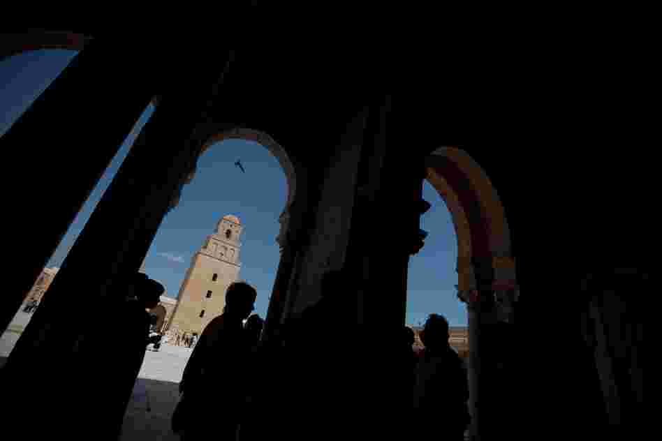 Kairouan is home to scores of places of worship, including the Great Mosque, a building of sandy bricks with a square minaret and a design that is said to have influenced mosques all through the region. Visitors and tourists are silhouetted inside the ancient building.