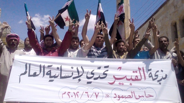 Anti-government protesters in the northern Syrian village of Hass protest on Thursday following the deaths of dozens of civilians a day earlier in the village of Mazraat al-Qubair. The banner reads, "The al-Qubair massacre challenges the world's humanity."
