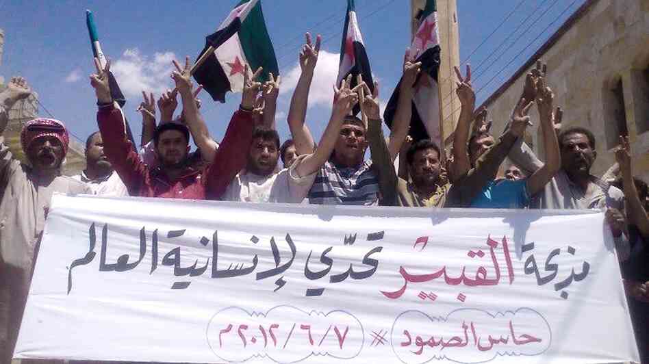 Anti-government protesters in the northern Syrian village of Hass protest on Thursday following the deaths of dozens of civilians a day earlier in the village of Mazraat al-Qubair. The banner reads, "The al-Qubair massacre challenges the world's humanity."