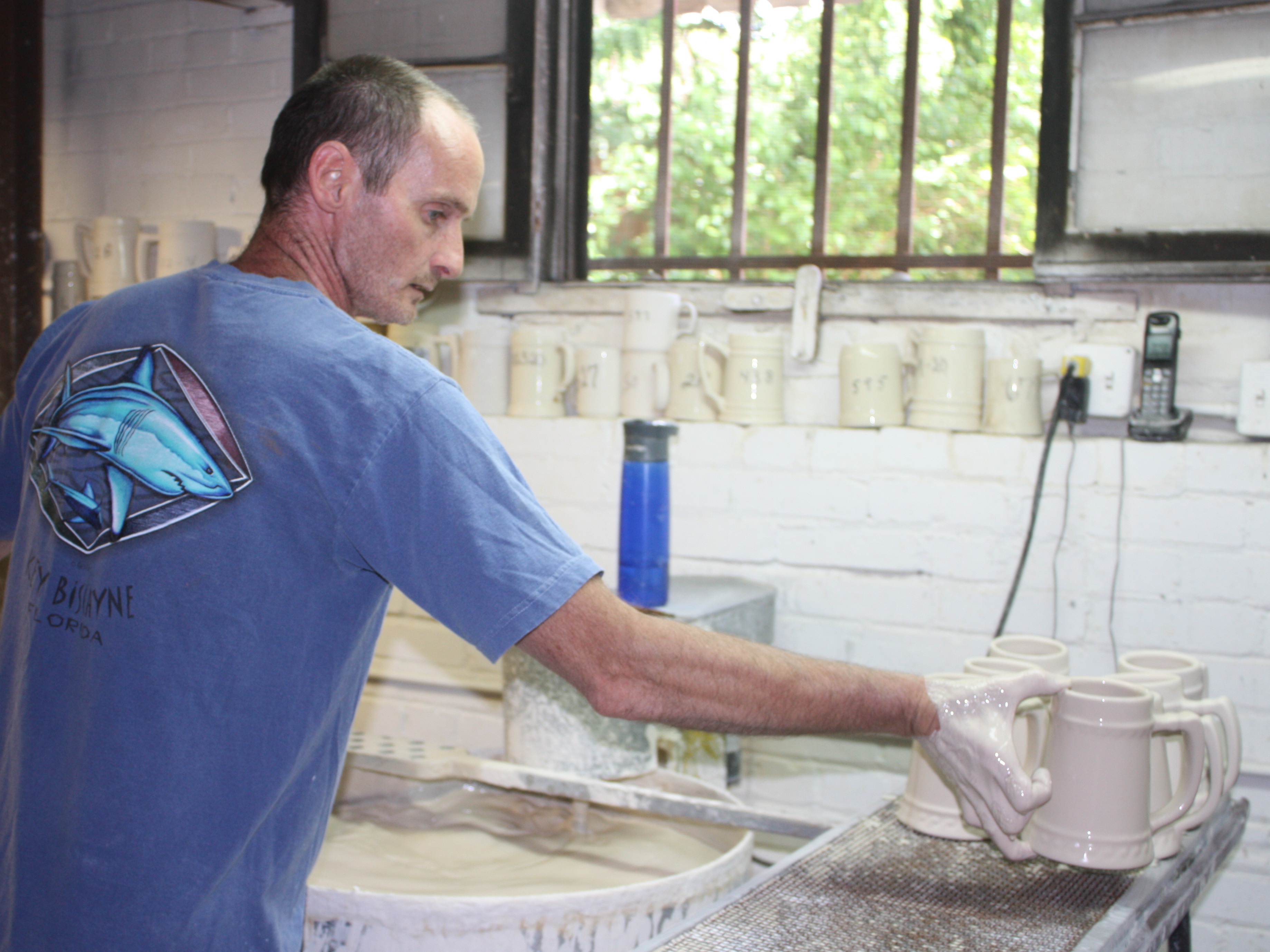 Bob Davis hand-dips mugs before they go into the kiln at American Mug and Stein in East Liverpool, Ohio. Most overseas companies have machines that can do this much faster. (Image credit: WKSU)