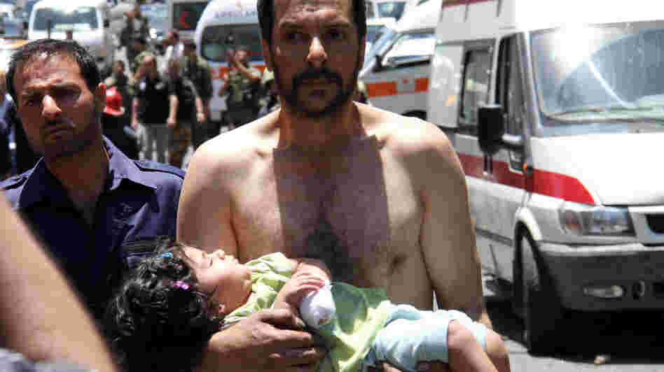 A Syrian man carries a wounded girl next to Red Crescent ambulances following an explosion Friday reportedly targeting a military bus near Qudssaya, a neighborhood in Damascus. A Syrian man carries a wounded girl next to Red Crescent ambulances following an explosion Friday reportedly targeting a military bus near Qudssaya, a neighborhood in Damascus.