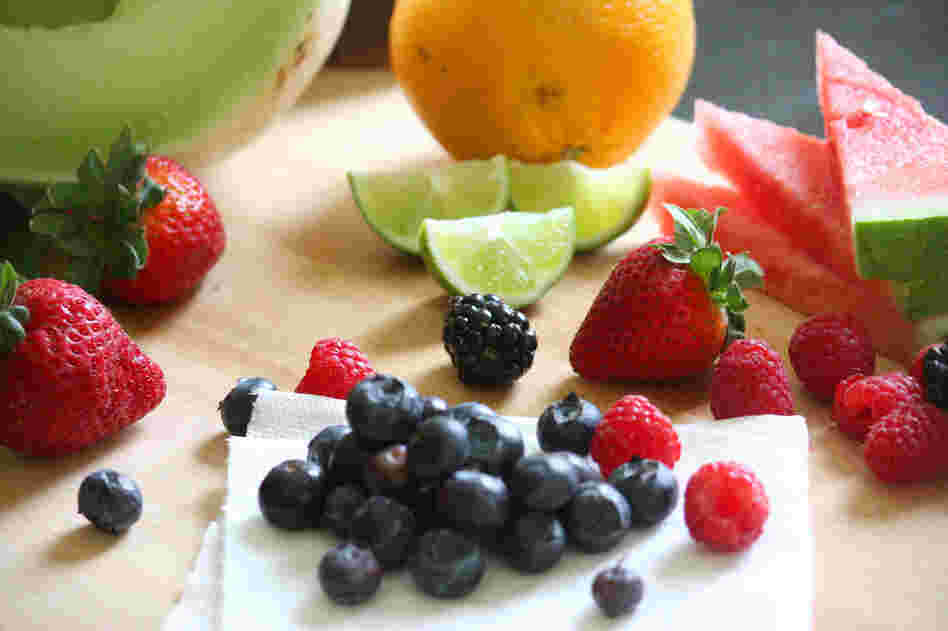 Fruit salad ingredients, including honeydew, watermelon, orange, lime, strawberries, blueberries and raspberries.