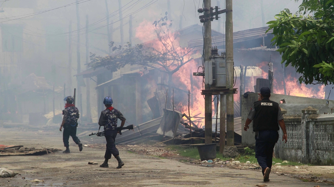 Policemen walk toward burning buildings in Sittwe, where some residents fled burning homes and gunshots as deadly ethnic violence broke out.