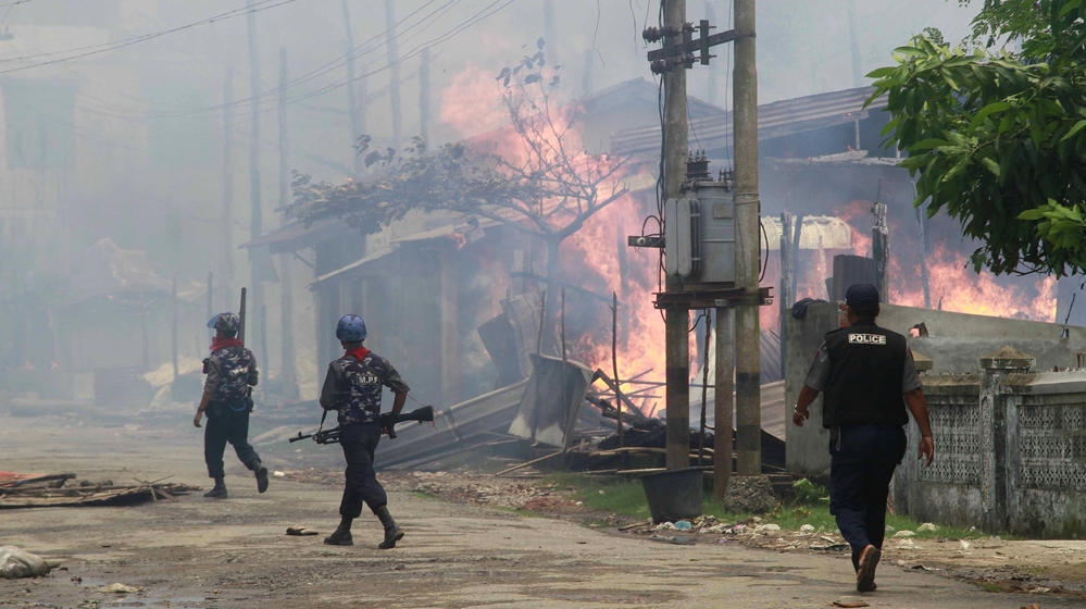Policemen walk toward burning buildings in Sittwe, where some residents fled burning homes and gunshots as deadly ethnic violence broke out.