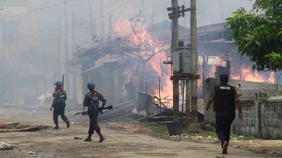 Policemen walk toward burning buildings in Sittwe, where some residents fled burning homes and gunshots as deadly ethnic violence broke out.
