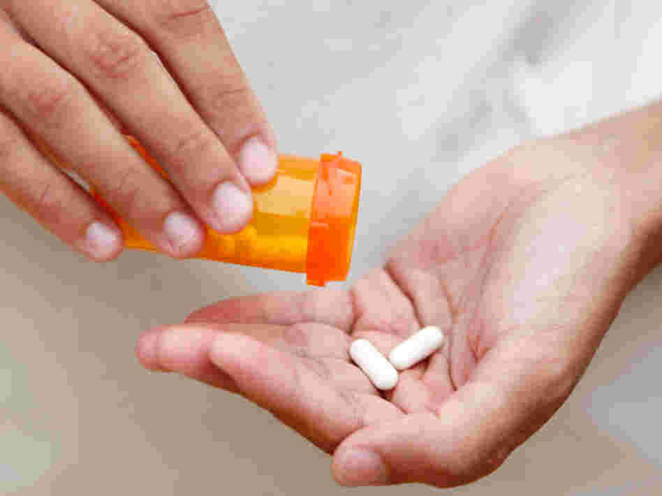 A woman pours two tablets into her hand from a pill bottle. A woman pours two tablets into her hand from a pill bottle.