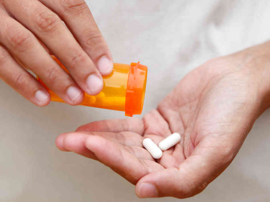 A woman pours two tablets into her hand from a pill bottle. A woman pours two tablets into her hand from a pill bottle.