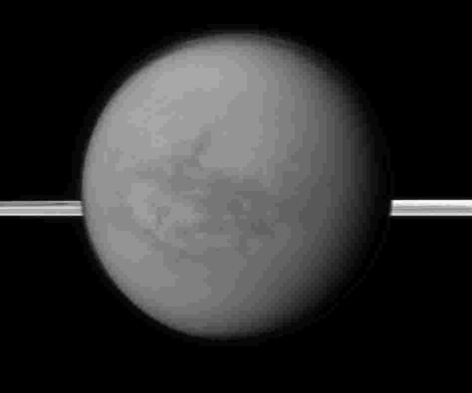 This image provided by NASA shows Titan with Saturn's rings in the background. A new study being released on Thursday suggests the dark areas near Titan's equator indicate the presence of a hydrocarbon lake and several ponds, a surprise to scientists who thought lakes only existed at the poles.