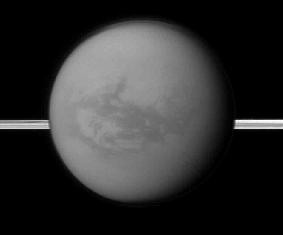 This image provided by NASA shows Titan with Saturn's rings in the background. A new study being released on Thursday suggests the dark areas near Titan's equator indicate the presence of a hydrocarbon lake and several ponds, a surprise to scientists who thought lakes only existed at the poles.