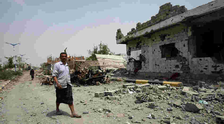 Yemeni residents walk past vehicles and houses which were destroyed during recent fighting between the army and militants on a road leading to the city of Zinjibar on Thursday.