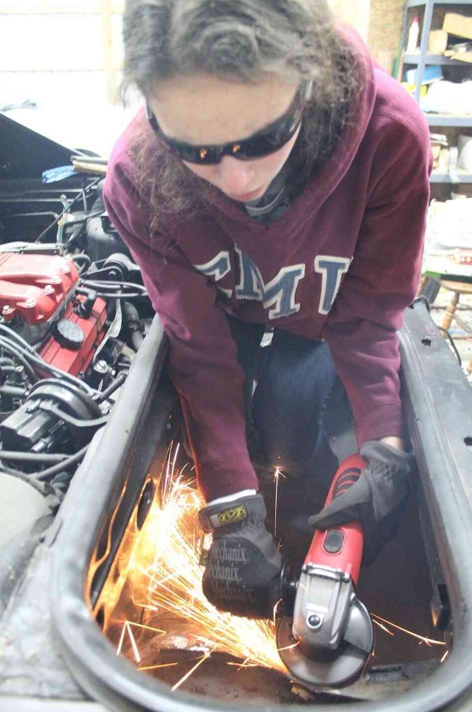 Kathryn DiMaria using her grinder to cut a hole in the trunk of her Pontiac Fiero. Kathryn DiMaria using her grinder to cut a hole in the trunk of her Pontiac Fiero.