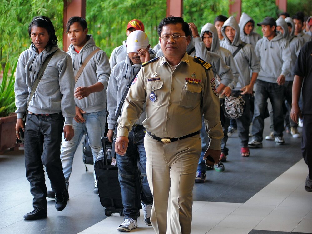 A Cambodian policeman escorts 30 fishermen returning home after being freed or escaping from slave-like conditions on Thai fishing vessels. The men arrived at the Phnom Penh airport in December. Large numbers of men from Myanmar and Cambodia are trafficked onto Thai fishing boats and forced to work in brutal conditions.