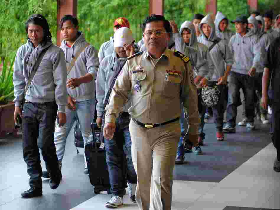 A Cambodian policeman escorts 30 fishermen returning home after being freed or escaping from slave-like conditions on Thai fishing vessels. The men arrived at the Phnom Penh airport in December. Large numbers of men from Myanmar and Cambodia are trafficked onto Thai fishing boats and forced to work in brutal conditions.