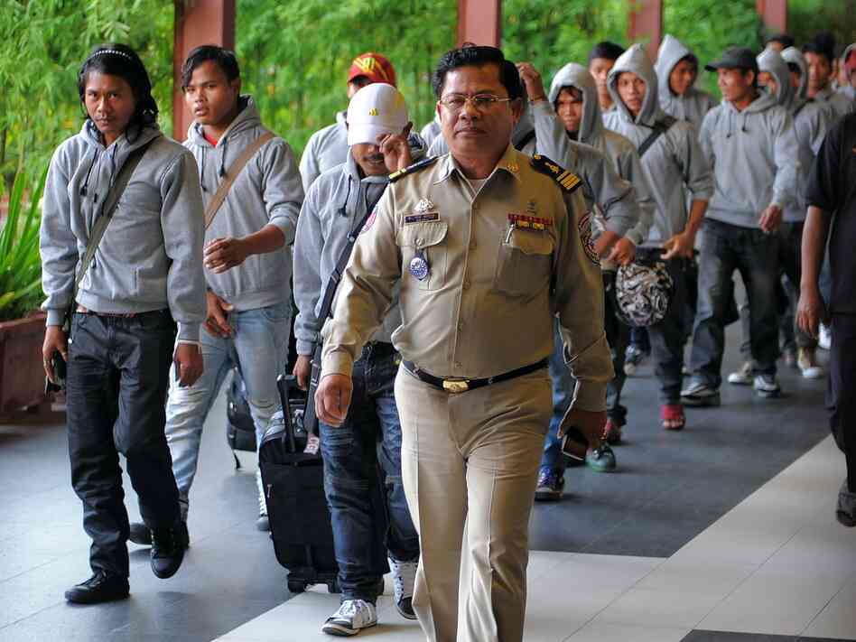 A Cambodian policeman escorts 30 fishermen returning home after being freed or escaping from slave-like conditions on Thai fishing vessels. The men arrived at the Phnom Penh airport in December. Large numbers of men from Myanmar and Cambodia are trafficked onto Thai fishing boats and forced to work in brutal conditions.