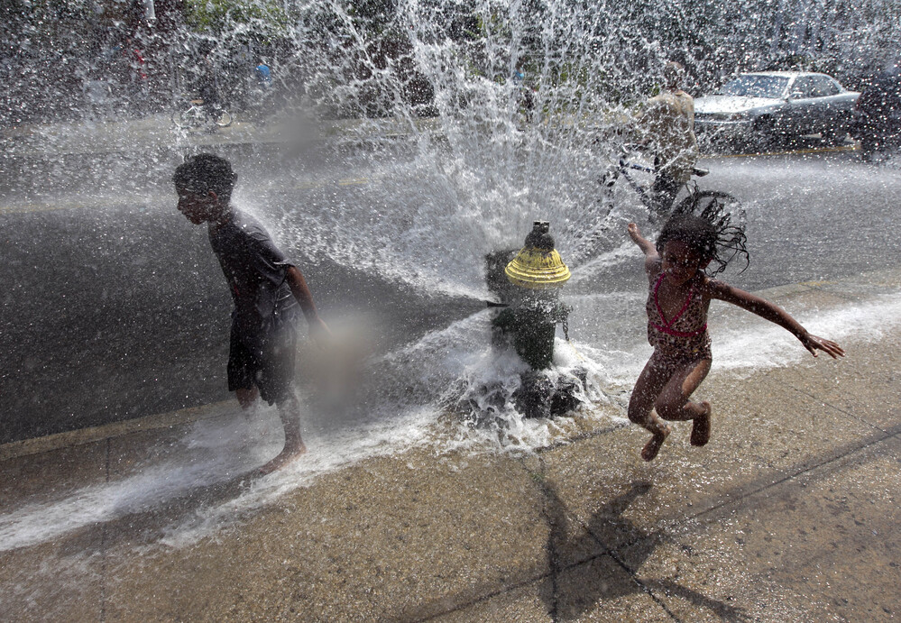 Four-year-old Solaris Arias, of Providence, R.I., right, jumps through water spraying from an open fire hydrant on Wednesday.
