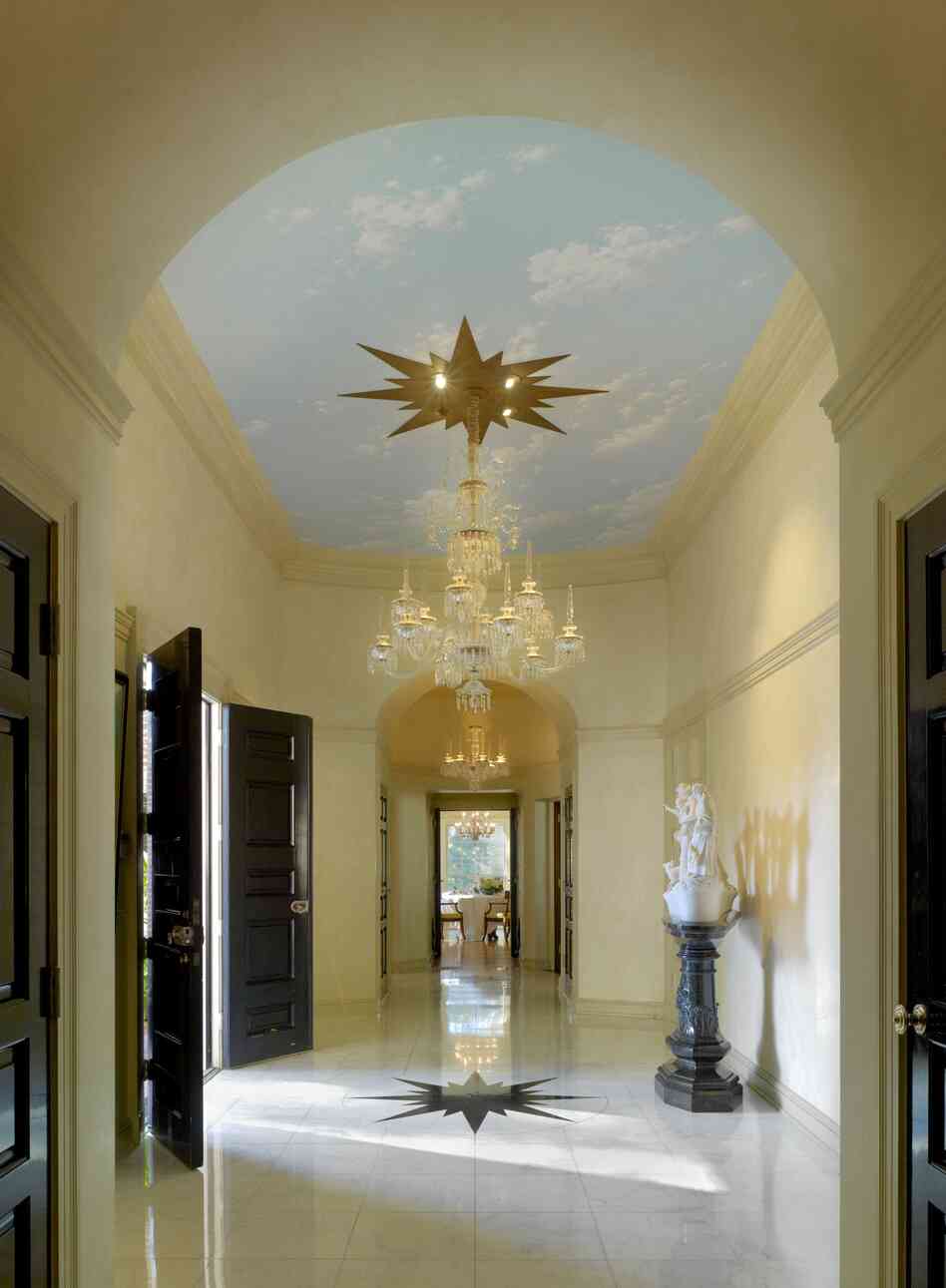 Williams thought a home's entrance should make a statement. In this Colonial Revival residence, designed in Beverly Hills for the Landis family in 1955, the narrow foyer has large double doors that swing open to reveal a high ceiling covered in a trompe l'oeil sky, and a lavish chandelier hung from a starburst medallion. The medallion's design is repeated on the marble floor.