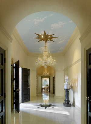 Williams thought a home's entrance should make a statement. In this Colonial Revival residence, designed in Beverly Hills for the Landis family in 1955, the narrow foyer has large double doors that swing open to reveal a high ceiling covered in a trompe l'oeil sky, and a lavish chandelier hung from a starburst medallion. The medallion's design is repeated on the marble floor.