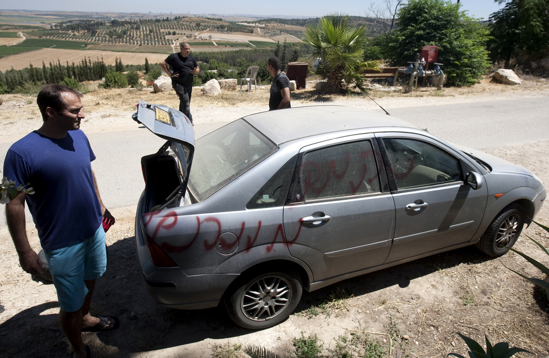 Vandals slashed car tires and spray-painted graffiti in the village of Neve Shalom earlier this month. Here, Jewish Israeli and Arab Israeli men inspect a car that was spray-painted with the word "Revenge."