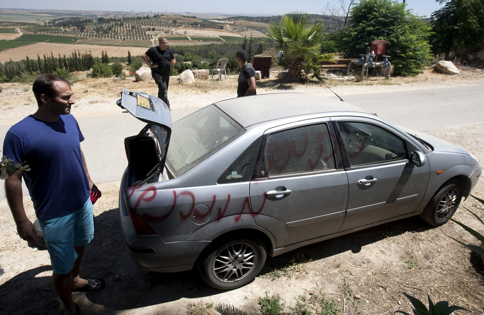 Vandals slashed car tires and spray-painted graffiti in the village of Neve Shalom earlier this month. Here, Jewish Israeli and Arab Israeli men inspect a car that was spray-painted with the word "Revenge."