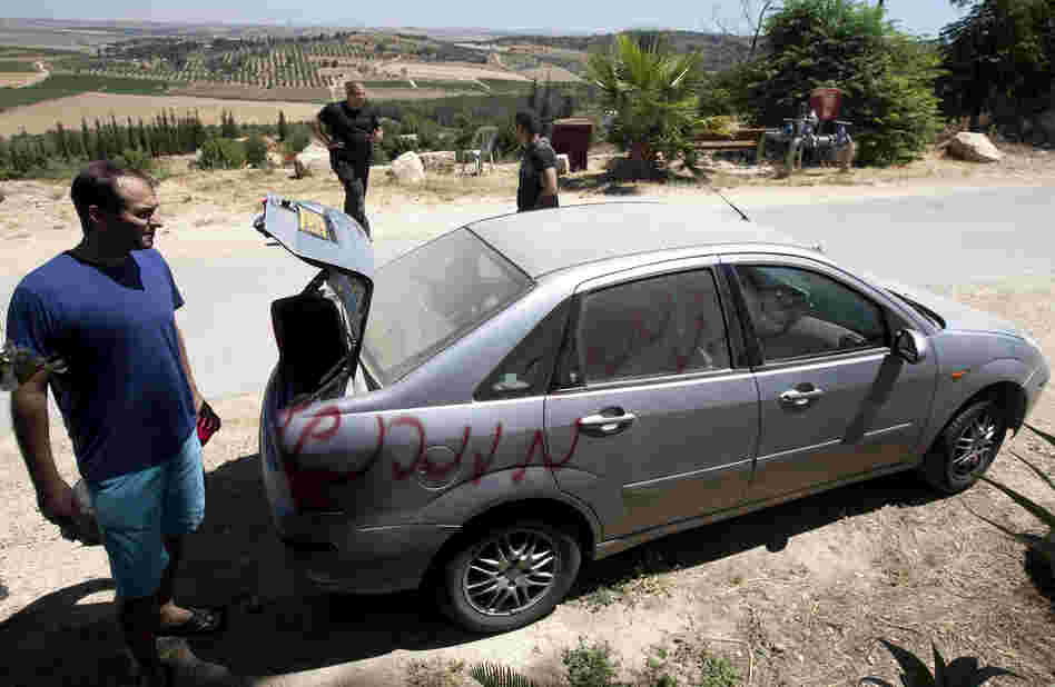 Vandals slashed car tires and spray-painted graffiti in the village of Neve Shalom earlier this month. Here, Jewish Israeli and Arab Israeli men inspect a car that was spray-painted with the word "Revenge."