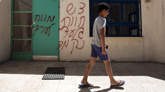 A boy walks past spray-painted graffiti that reads in Hebrew, "Death to Arabs" and "Revenge." The vandalism took place earlier this month in the mixed Arab-Jewish community of Neve Shalom in Israel.
