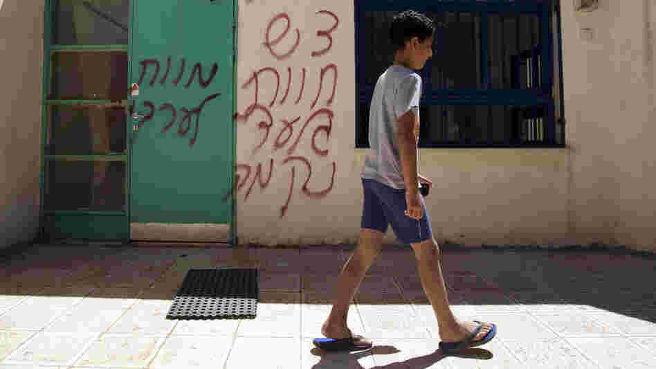 A boy walks past spray-painted graffiti that reads in Hebrew, "Death to Arabs" and "Revenge." The vandalism took place earlier this month in the mixed Arab-Jewish community of Neve Shalom in Israel.