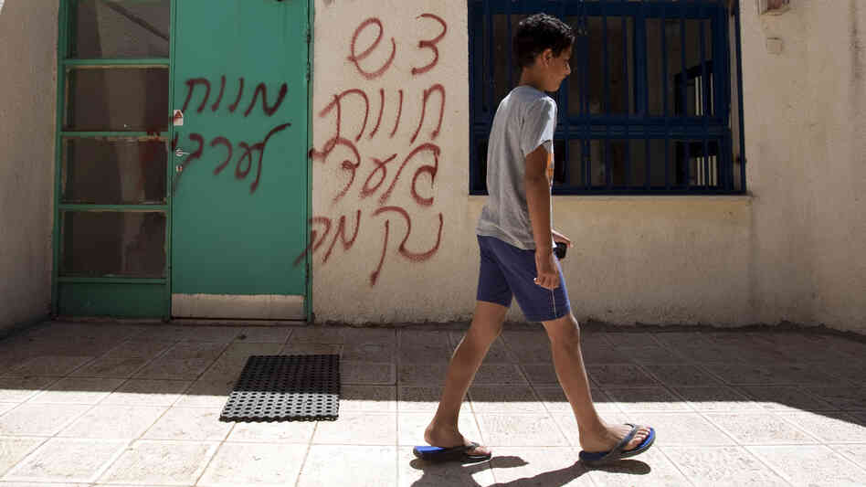 A boy walks past spray-painted graffiti that reads in Hebrew, "Death to Arabs" and "Revenge." The vandalism took place earlier this month in the mixed Arab-Jewish community of Neve Shalom in Israel.