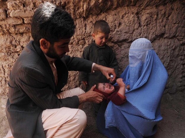Many Afghan government programs depend on foreign aid. Here, an Afghan health worker administers a polio vaccine to a child in the western province of Herat on March 27.