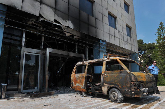 A security officer stands by the van used by attackers at the entrance of the Microsoft office in an Athens on Wednesday.