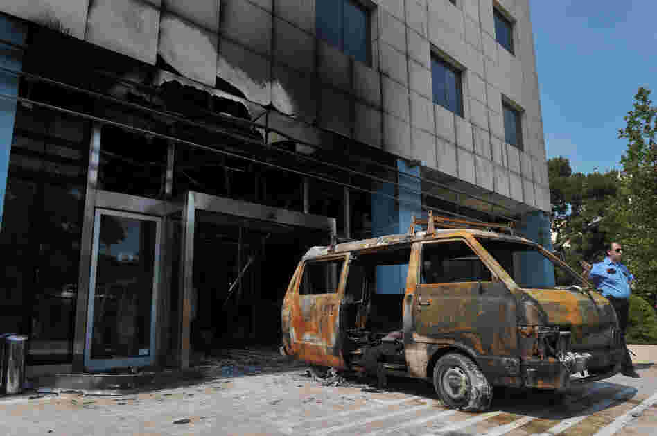 A security officer stands by the van used by attackers at the entrance of the Microsoft office in an Athens on Wednesday.