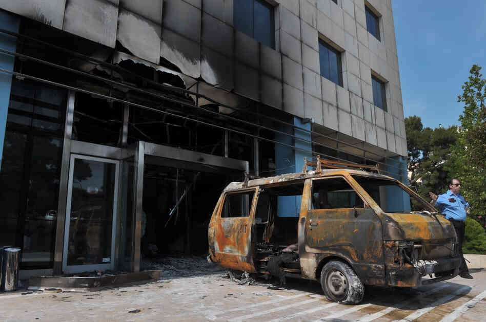 A security officer stands by the van used by attackers at the entrance of the Microsoft office in an Athens on Wednesday.