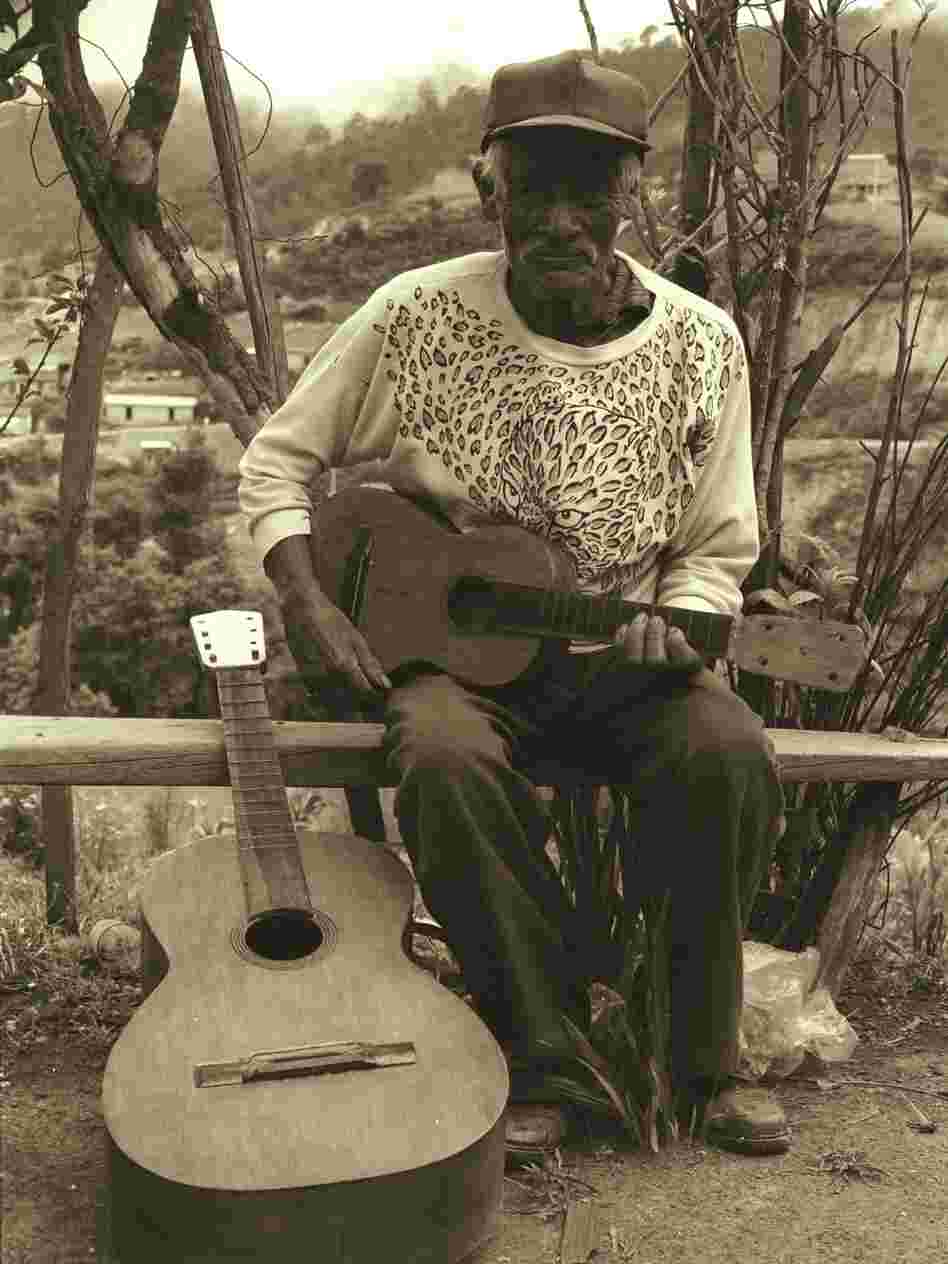 Don Telesforo next to a bajo quinto, holding a jarana mixteca.