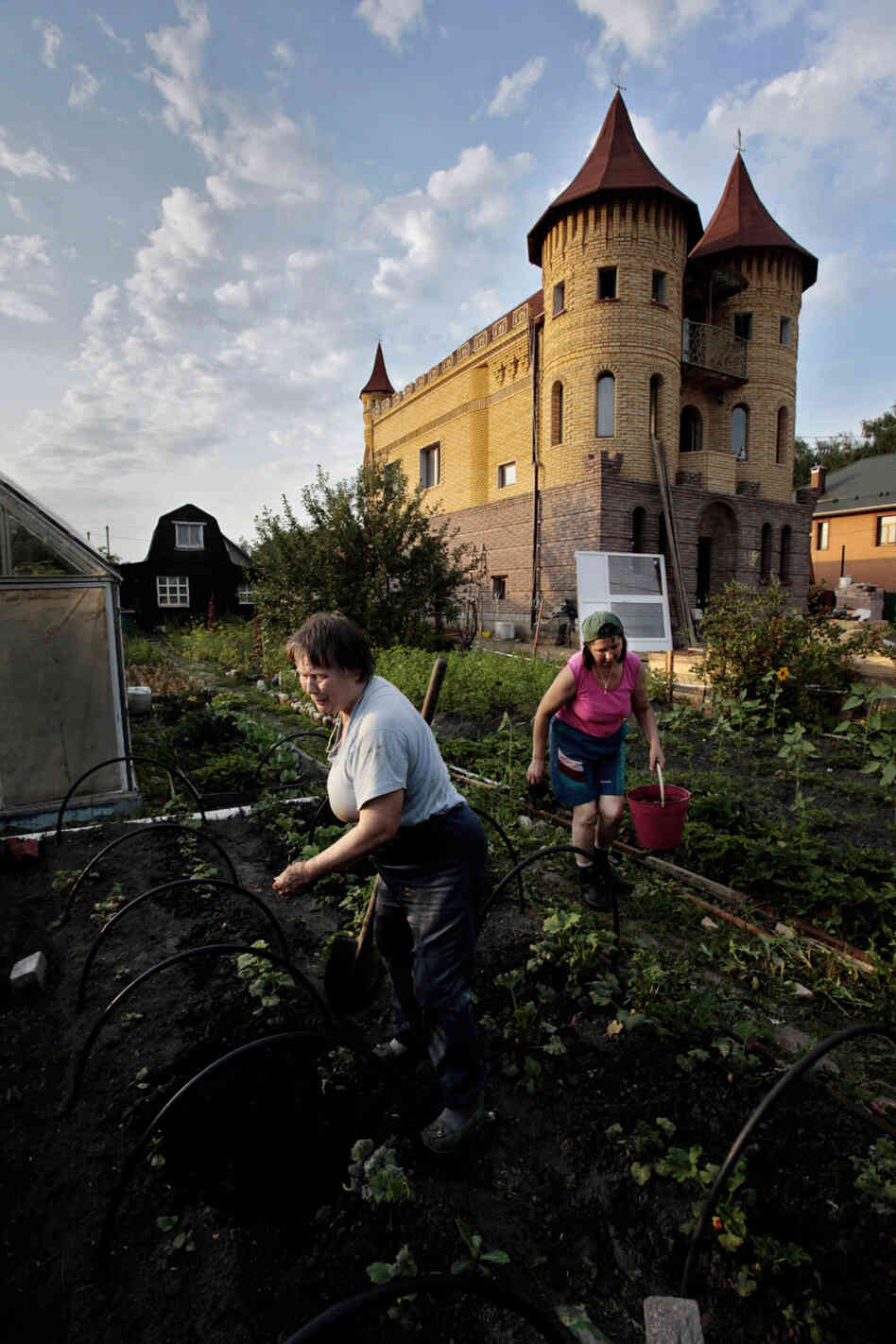In the mishmash of a dacha community, an ersatz schloss and wooden shack may stand shoulder to shoulder. Here, Zinaida Kondratyeva, owner of the modest wood house in the background, works with her daughter-in-law in her garden near Moscow. The castle-like house is owned by a lawyer.