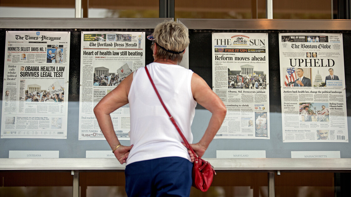 Joy Reynolds of San Diego, Calif., looks over Friday's front pages on display at the Newseum in Washington, the day after the Supreme Court ruling on President Barack Obama's health care law.