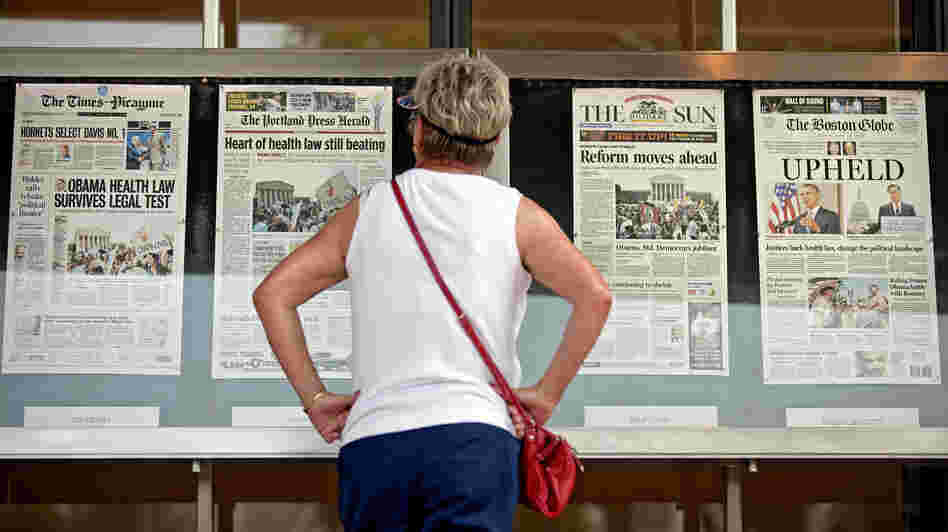 Joy Reynolds of San Diego, Calif., looks over Friday's front pages on display at the Newseum in Washington, the day after the Supreme Court ruling on President Barack Obama's health care law.