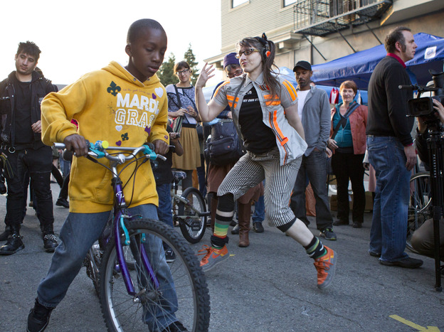 A performance artist dances on 23rd Street in Oakland as First Friday Art Walk attendees pass by.