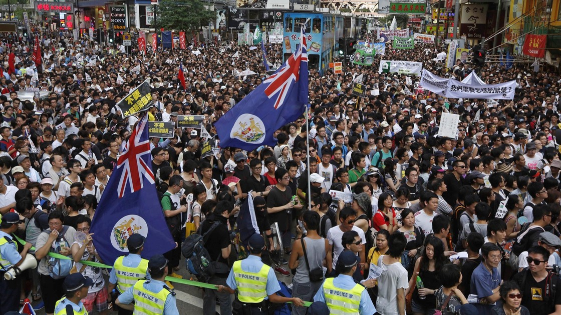 Flags from Hong Kong's colonial period fly over crowds in Victoria park on Sunday.Huge crowds pack Hong Kong's Victoria park, marching through the city's streets Sunday to express their dissatisfaction with the new leader.