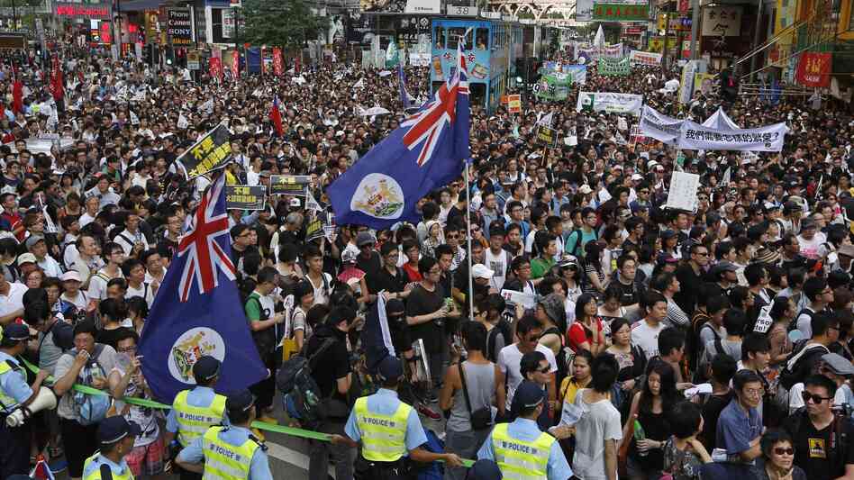 Flags from Hong Kong's colonial period fly over crowds in Victoria park on Sunday.Huge crowds pack Hong Kong's Victoria park, marching through the city's streets Sunday to express their dissatisfaction with the new leader.