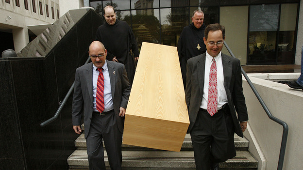 Deacon Mark Coudrain, bottom left, Rev. Charles Benoit, top left, Abbot Justin Brown, top right, and attorney Evans Schmidt carry a casket built by Benedictine monks down the steps of the U.S. federal district courthouse on Aug. 12, 2010.