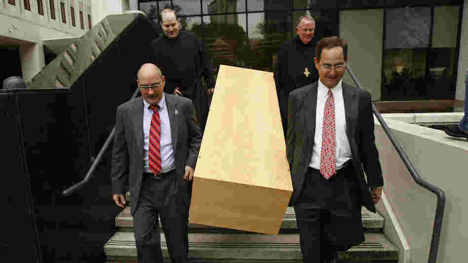 Deacon Mark Coudrain, bottom left, Rev. Charles Benoit, top left, Abbot Justin Brown, top right, and attorney Evans Schmidt carry a casket built by Benedictine monks down the steps of the U.S. federal district courthouse on Aug. 12, 2010.