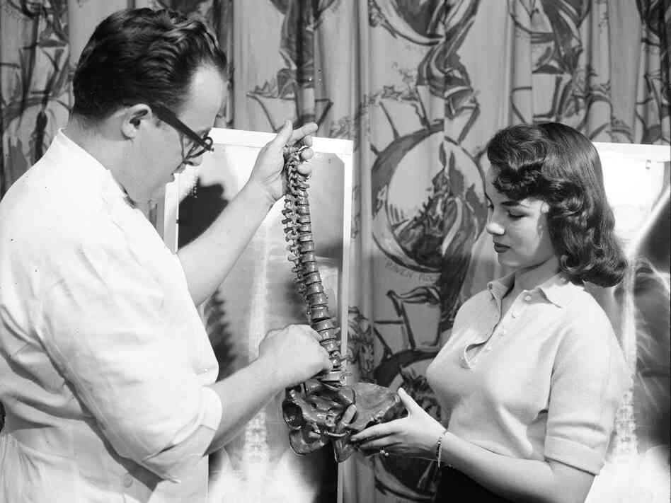 Lois Conway stands by her spinal X-ray and reviews a model of the human spine with a chiropractor.