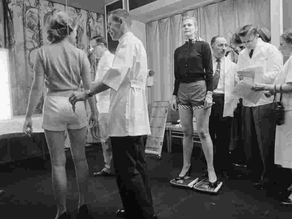 How straight is her spine? A chiropractor uses a plumb bob to find out. Across the room another contestant straddles two scales so chiropractors can evaluate her posture.