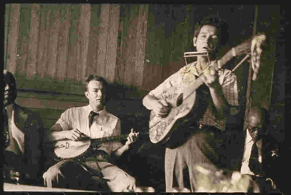 Guthrie plays his signature guitar with "This machine kills fascists" scrawled across the front. Pete Seeger accompanies on banjo; music journalist Dan Burley sits at left.