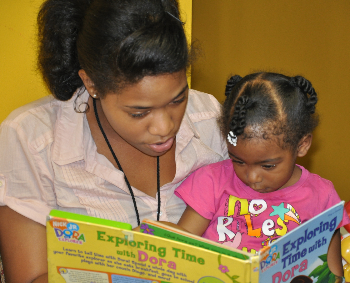 A volunteer reads a book with a visitor at The Homeless Children's Playtime Project.